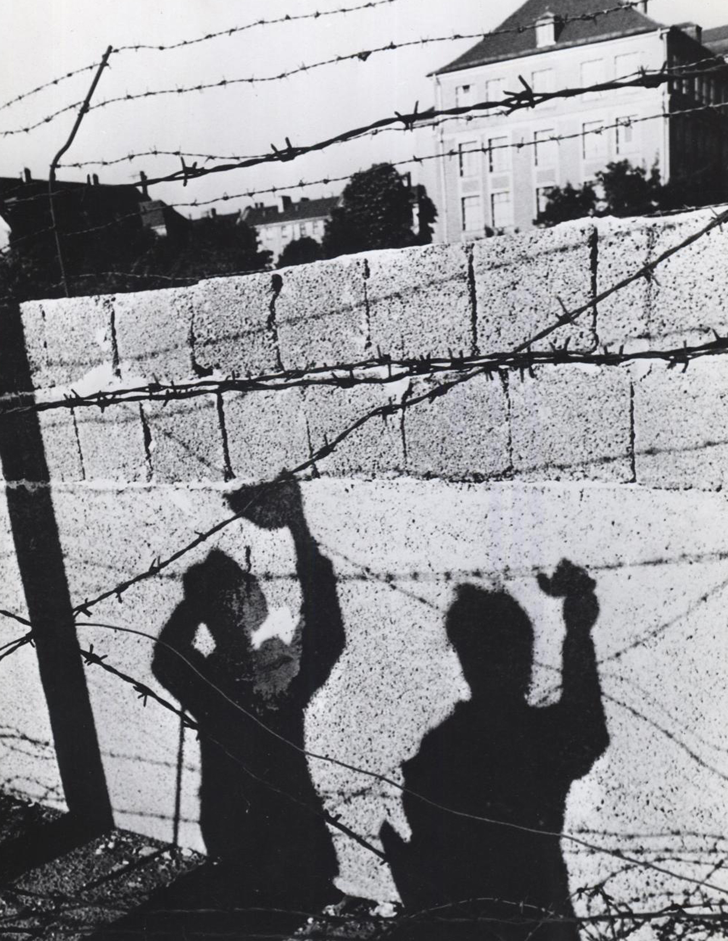 A picture is worth a thousand words: In October 1961, the shadows of two West Berliners waving to friends across the East-West border fall symbolically upon the concrete of the newly-built wall in a frame of barbed wire. Photo: U.S. Information Agency.